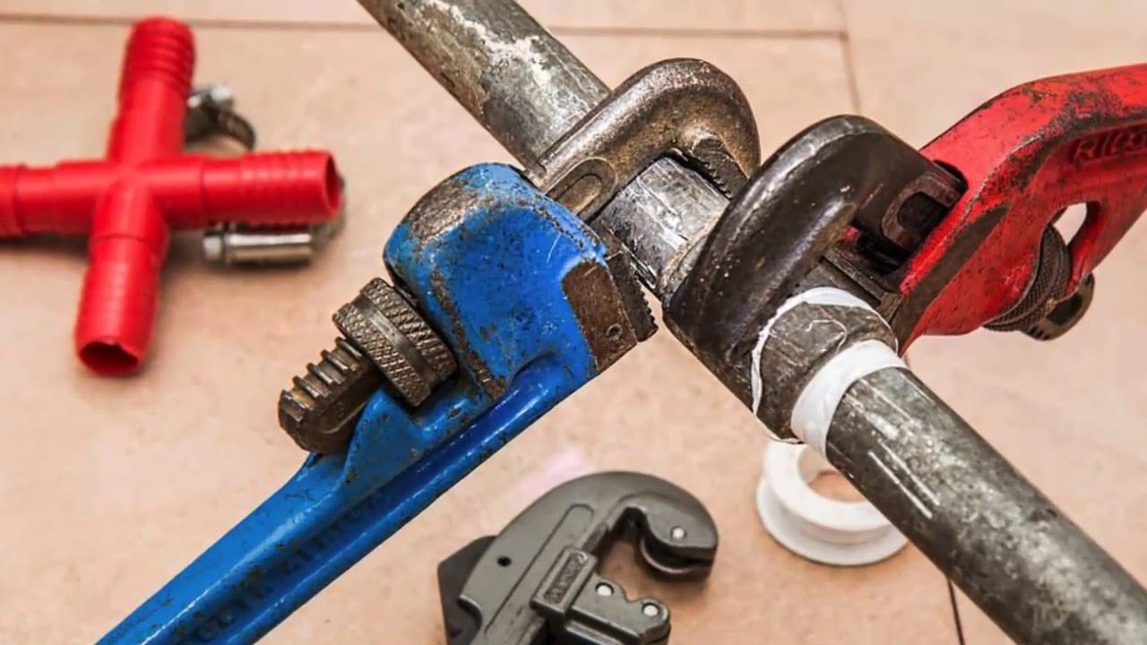 Blue and red pipe wrenches gripping a metal pipe, surrounded by plumbing tools and fittings, illustrating plumbing work in Sutherland Shire.