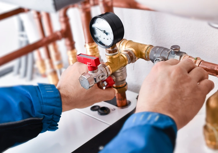 A licensed gas plumber inspecting and adjusting brass pipe fittings and a pressure gauge on a copper gas system.