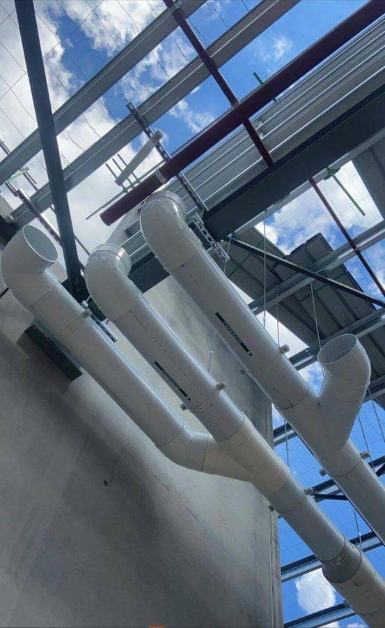 White industrial pipes in a modern plumbing facility with large glass windows and bright blue sky.