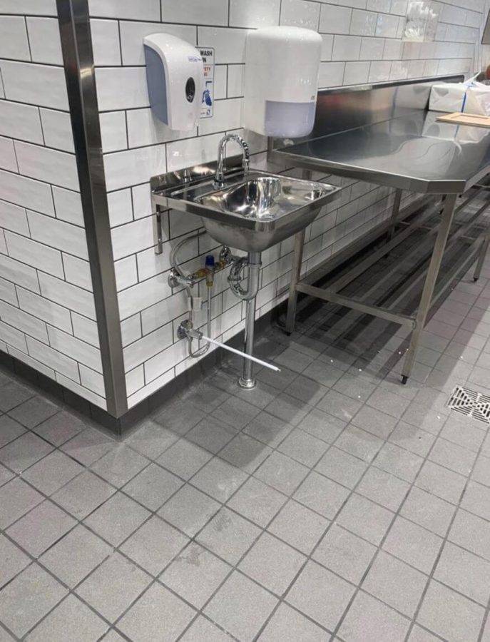 Stainless steel commercial sink and hand dryer in a modern plumbing workspace with paper towel dispenser.