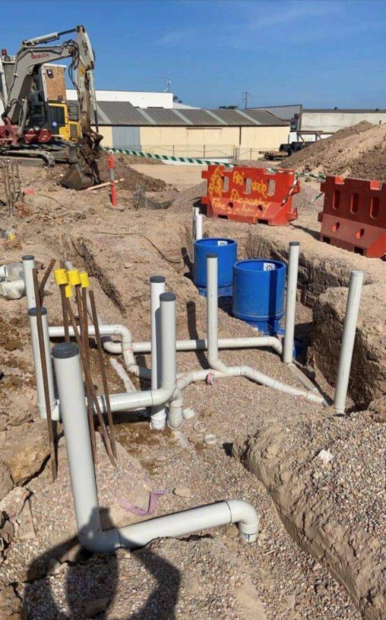 Construction site with underground piping and drainage by Priority Plus Plumbing, featuring machinery and safety barriers.