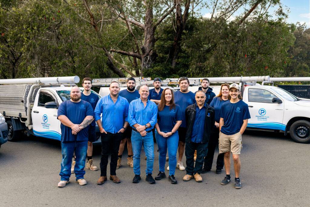 Priority Plus Plumbing team in blue uniforms standing near service vehicles in Sutherland Shire.